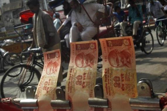 Cycle rickshaws move past a display of Indian rupees at a roadside currency exchange stall in the old quarters of Delhi