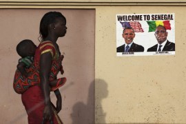 A woman carrying her baby on her back walks past a poster of U.S. President Obama and Senegal''s President Sall before Obama''s visit in Dakar