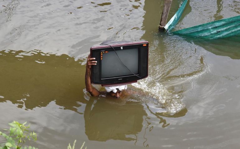 A flood-affected man carries his television set to a safer place in the northern Indian city of Allahabad