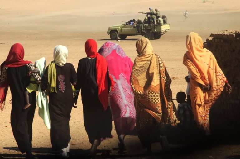 Women and children walk near a truck carrying government troops in Tabit, north Darfur