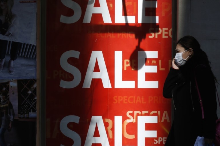 A woman holding her mobile phone walks past a sales advertisement poster in front of a shoes store in Tokyo
