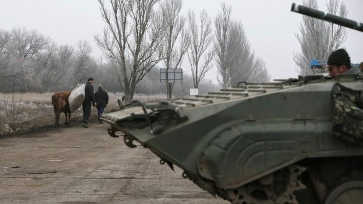 Member of the Ukrainian armed forces pilots a military vehicle as local residents walk with their cow on the road near Artemivsk