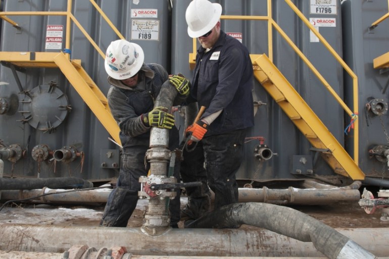 File photo of Torres and Anderson of Select Energy Services connecting hoses between a pipeline and water tanks at a Hess fracking site near Williston