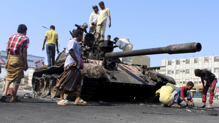 People gather near a tank burnt during clashes on a street in Yemen''s southern port city of Aden