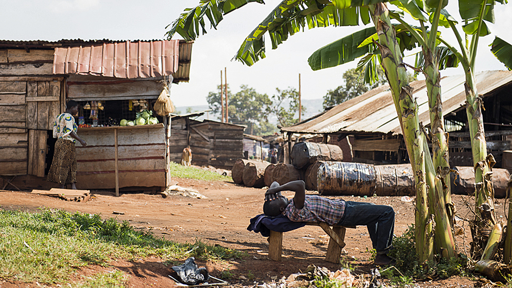 A drinker nurses his hangover in the shade of a banana tree. Imelda, a local distiller reveals 'the men around Kimasa drink all day and do no work' [AJ Heath/Al Jazeera]