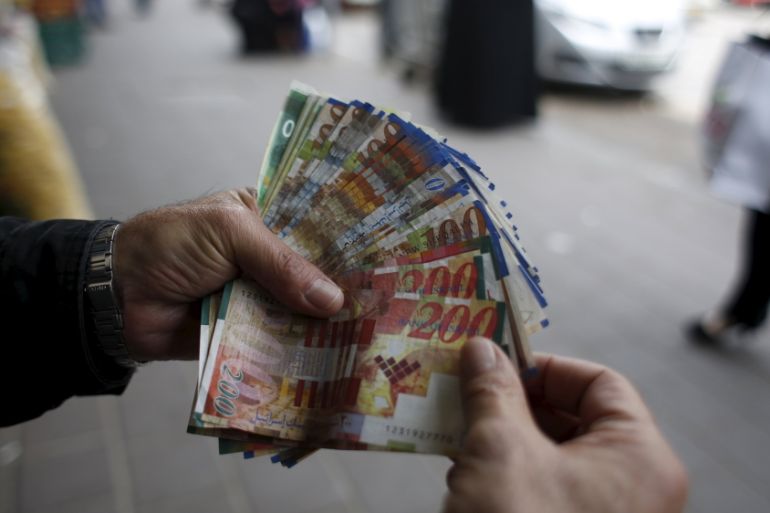 Palestinian money exchanger displays money at a market in the West Bank city of Ramallah