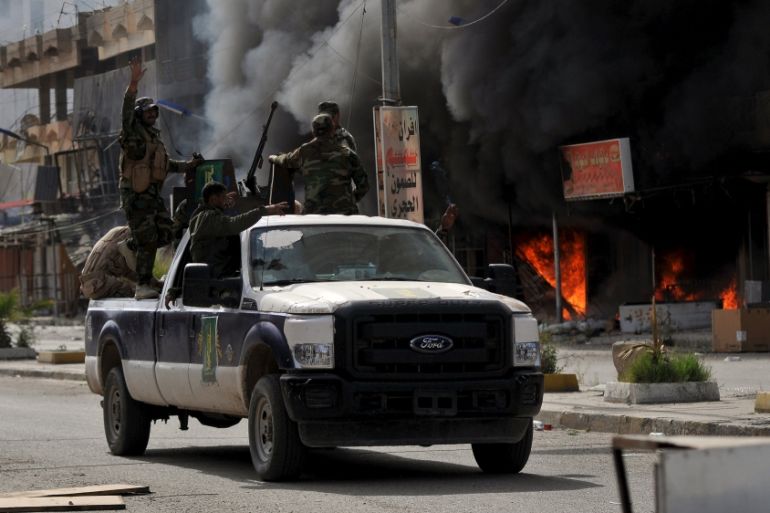 Members of Hashid Shaabi forces ride in a vehicle as smoke rises in shops at al-Qadisiya neighborhood, north of Tikrit
