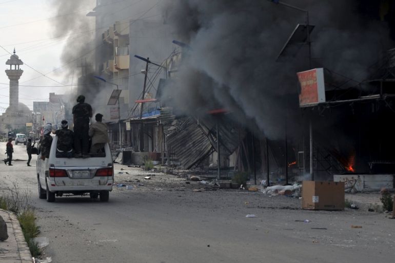 Members of Hashid Shaabi forces ride in a vehicle as smoke rises in shops at al-Qadisiya neighborhood, north of Tikrit