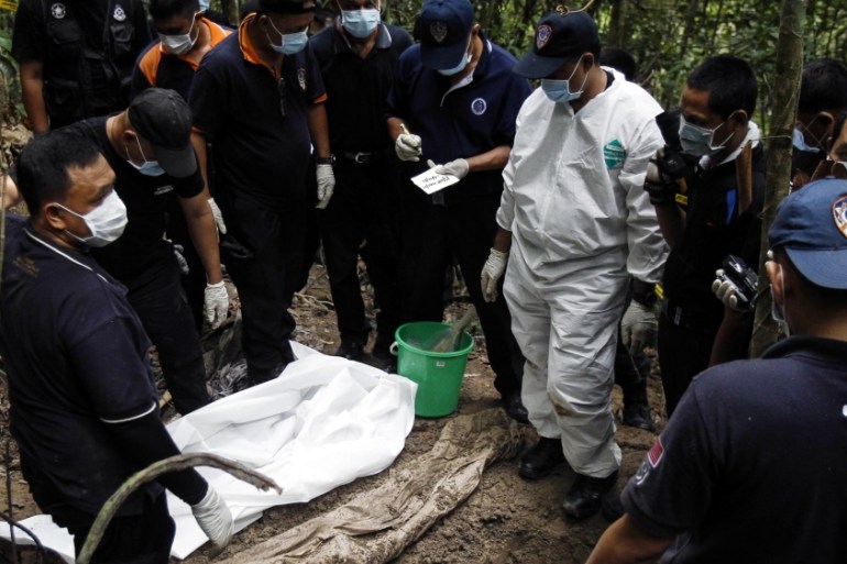 Malaysian police forensic team members inspect a freshly exhumed human body