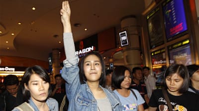 Thai pro-democracy activist Nacha Kong-udom flashes a three-finger salute as she is detained by female plain clothed police officers at a cinema in Bangkok [EPA] 