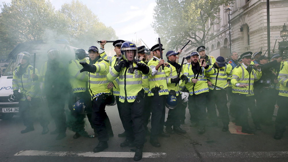 Police officers raise their batons as a smoke bomb goes off at the gates of Downing Street [Reuters]