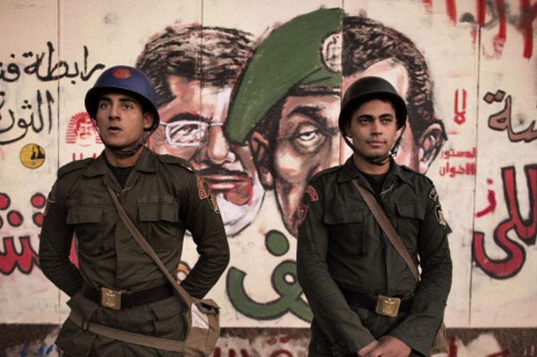 Egyptian soldiers stand in front of a graffiti on the walls of the Presidential Palace in Cairo [AFP]
