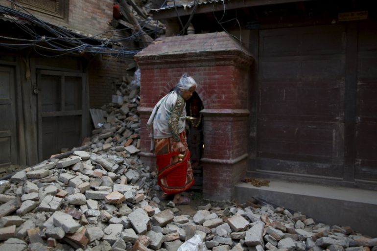 A woman walks on top of debris of a collapsed house as she returns after offering daily prayers at a temple, a month after the earthquake in Kathmandu, Nepal [REUTERS]