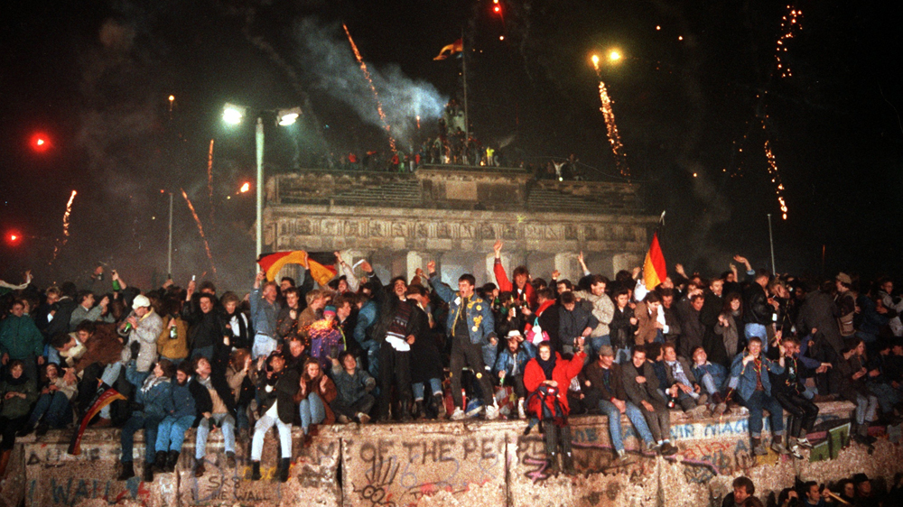 People are sitting and standing on the Berlin Wall in front of the Brandenburger Tor celebrating the new year and the opening of the wall [DPA]