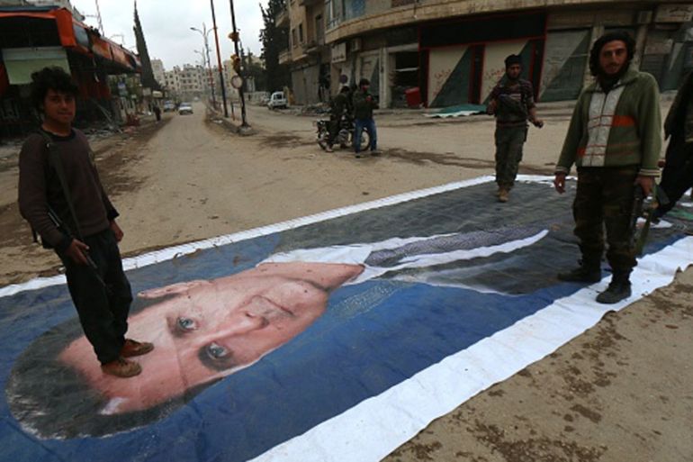 Fighters from a coalition of Islamist forces stand on a huge portrait of Syrian President Bashar al-Assad in Idlib [AFP]
