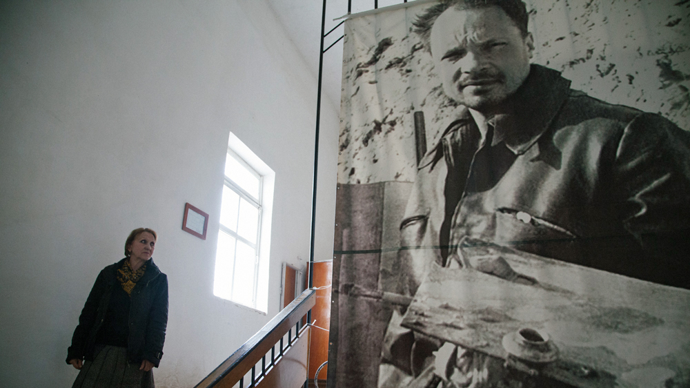 Chief curator Valentina Sycheva walks next to the portrait of Igor Savitsy, the founder of the Nukus Art Museum that now bears his name [Timur Karpov/Al Jazeera]