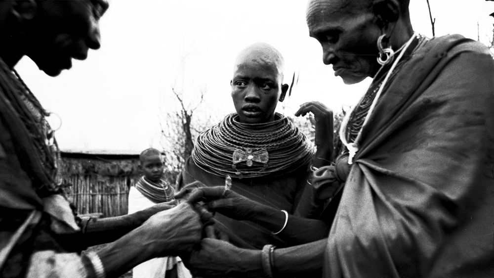 A bracelet made from goat's skin is put around Juliana's wrist by the woman who will perform the excision, left, and a relative, the day before her FGM. The 'circumciser' was legally blind but said she had been performing these rituals for so long that she could just feel where the cuts needed to be made [Mariella Furrer]