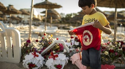 A boy holds a Tunisian flag as he stands near flowers laid at the beachside of the hotel attacked by a gunman in Sousse [REUTERS]