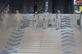 Workers wearing protective gears fumigate and spray antiseptic solution as a precaution against the spr