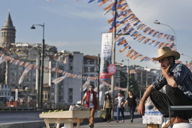 FILE - In this Tuesday, May 26, 2015 file photo, a street vendor is backdropped by the iconic Galata Tower and party flags and banners for the upcoming elections, as he waits for customers, in Istanbu