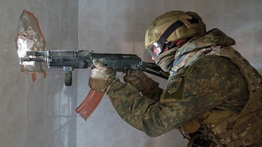 A soldier from the Azov regiments aims his rifle through a hole in the wall of a hotel, now used as a defence position on the front line [Christopher Allen/Al Jazeera]