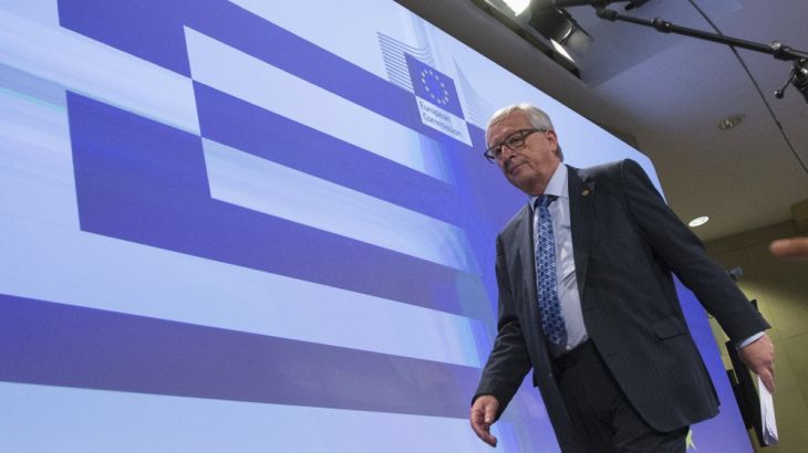 European Commission President Jean-Claude Juncker walks past a giant Greek flag projected in the press room after a statement on the situation on the situation in Greece in Brussels