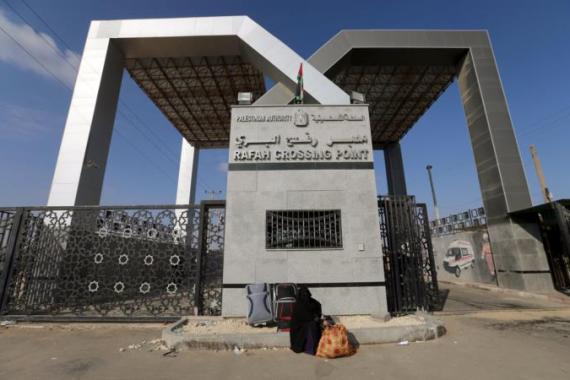 Palestinian woman sits in front of the gate of Rafah border crossing as she waits for a travel permit to cross into Egypt, in Rafah in the southern Gaza Strip