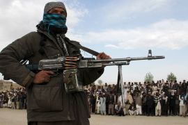 A member of the Taliban insurgent and other people stand at the site during the execution of three men in Ghazni Province