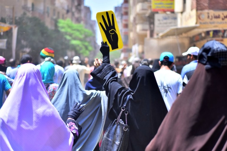 Female supporters of the Muslim Brotherhood gesture and hold up a sign picturing a hand with four fingers, a symbolic gesture of the deadly crackdown on MB supporters at two sit