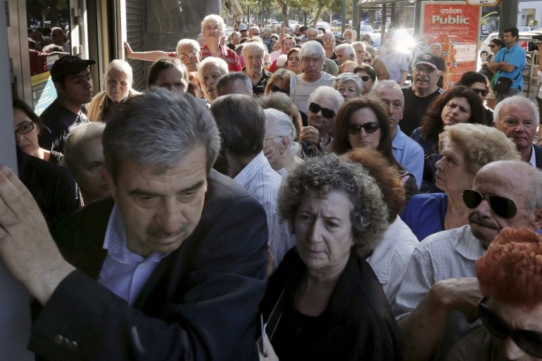 A manager tries to close the door of a bank as hundreds of pensioners line up outside a National Bank in Athens
