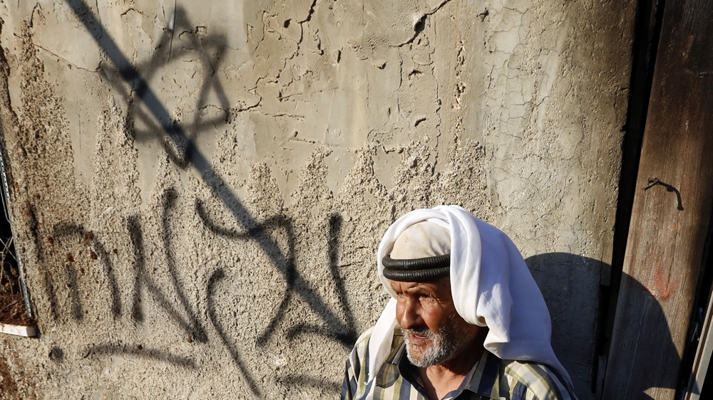 A Palestinian man stands infront of the fire damage to his son's house with graffiti reading in Hebrew 'revenge' in the West Bank [EPA]