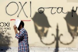 A man shelters from the sun as he walks past graffiti that reads "No" in Greek in Athens [REUTERS]
