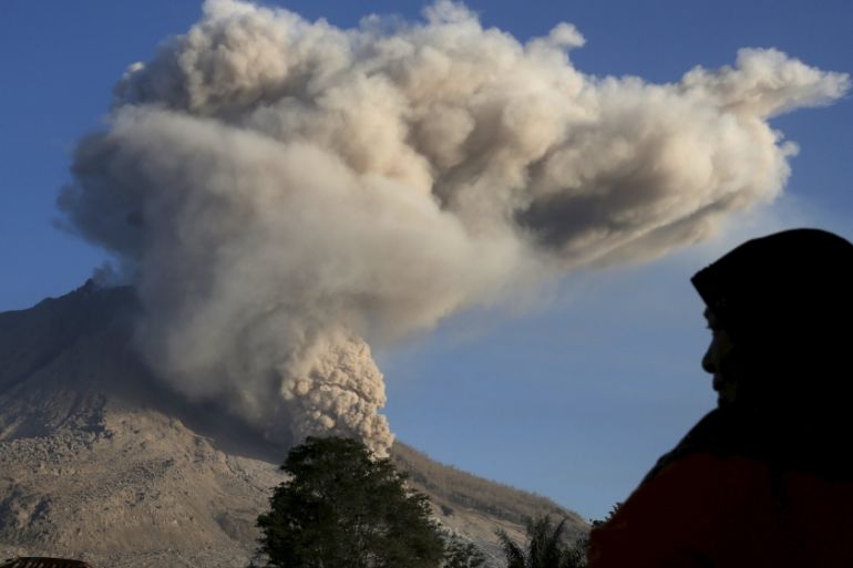 A woman looks as ash spews from Mount Sinabung volcano during an eruption at Kuta Tengah village in Karo Regency
