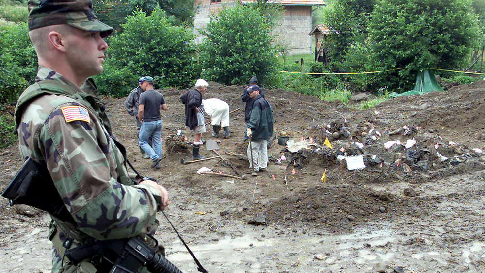 A US soldier serving with the NATO-led peacekeeping force in Bosnia patrols while Bosnian forensic experts inspect bodily remains found in a mass grave in the eastern village of Kamenica, near the town of Zvornik [Danilo Krstanovic/Reuters]
