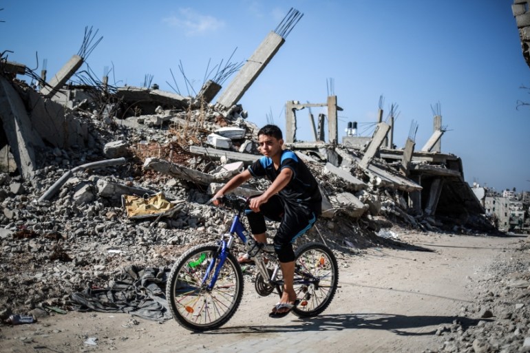 A boy ride a bike near the debris of buildings in the Shuja''iyya neighborhood, which was badly damaged in Israel''s most recent attacks on the Gaza strip, in Gaza City [Getty]