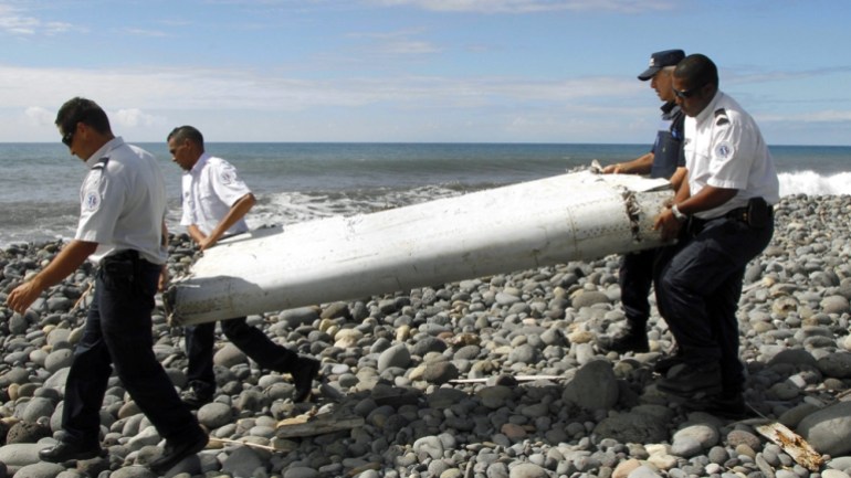 Four men carry a flaperon on a pebbly beach on Reunion Island. It was later identified as from MH370
