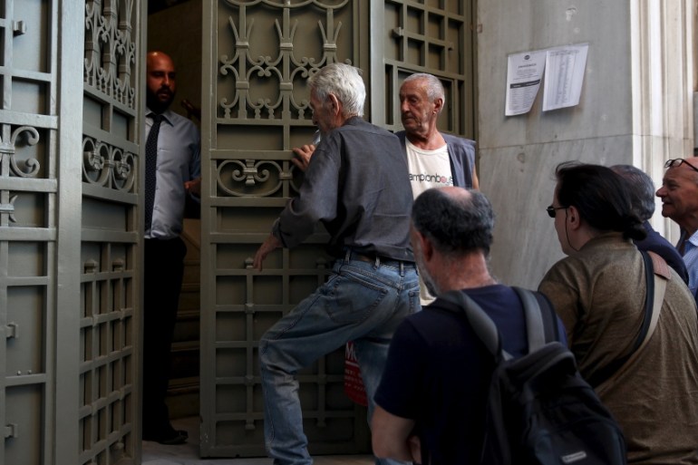 A National Bank official opens the door of a bank branch while people wait to enter in Athens