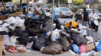 Pedestrians and motor vehicles pass by rubbish piled up along a street in Beirut [REUTERS]