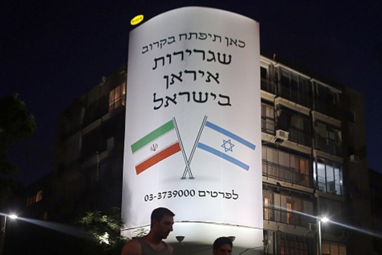 People walk past a large billboard depicting both national flags of Israel and Iran reading ''The Iranian embassy in Israel will open soon'' in central Tel Aviv [AFP]