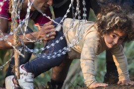 A refugee girl moves under barbed wire as she crosses from Serbia to Hungary [AP]
