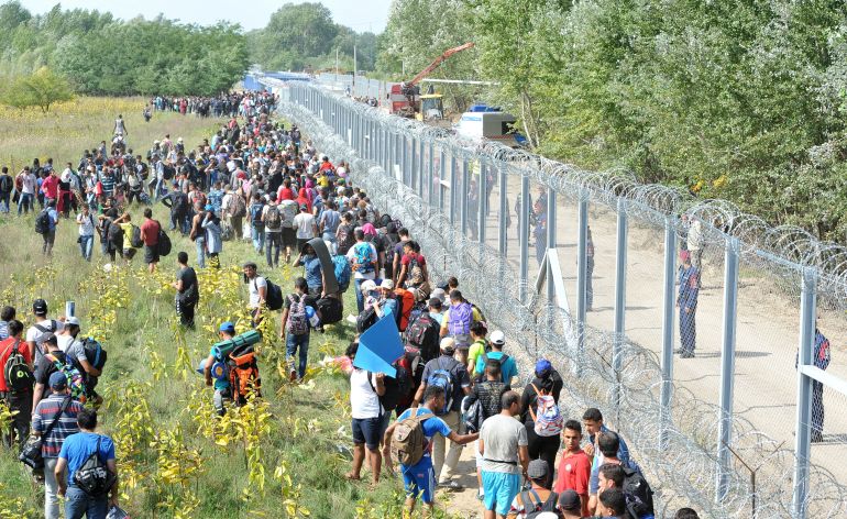 Migrants walk next to the razor wire fence at the Serbia-Hungary border