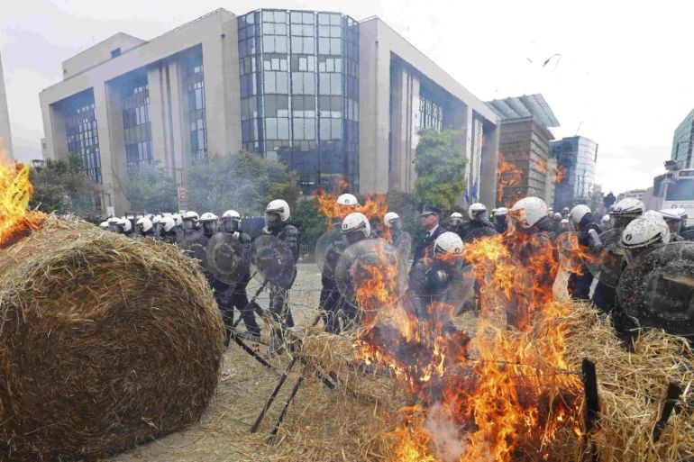 Belgian riot police officers stand guard as demonstrators burn hay