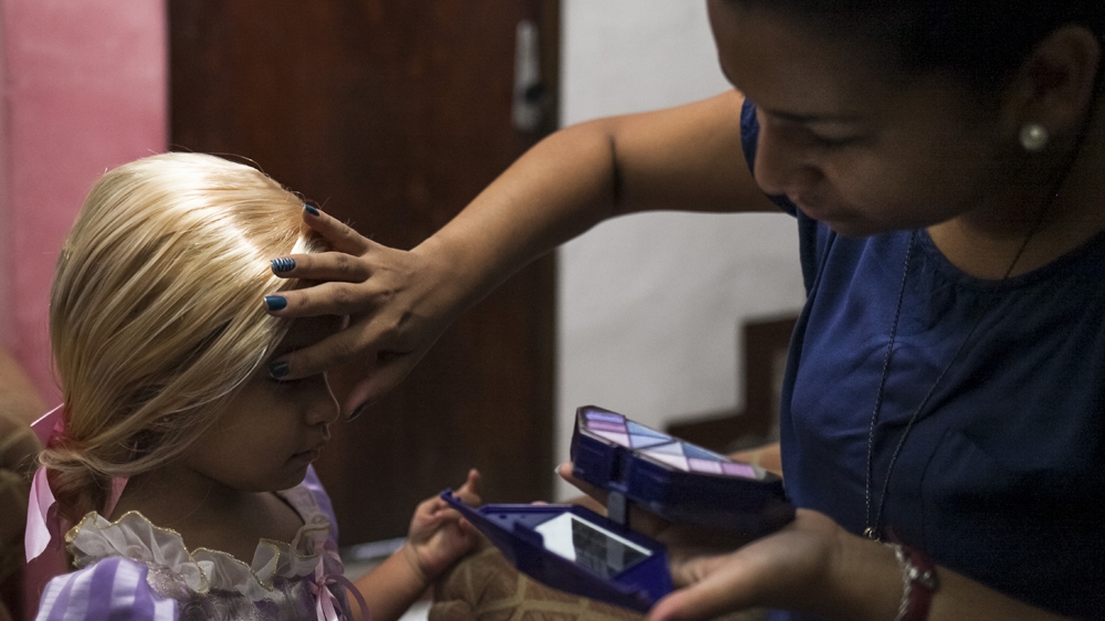 Carla applies make-up to her daughter, Sofia, who is attending a fancy dress party as Rapunzel [Santi Donaire/Al Jazeera] 