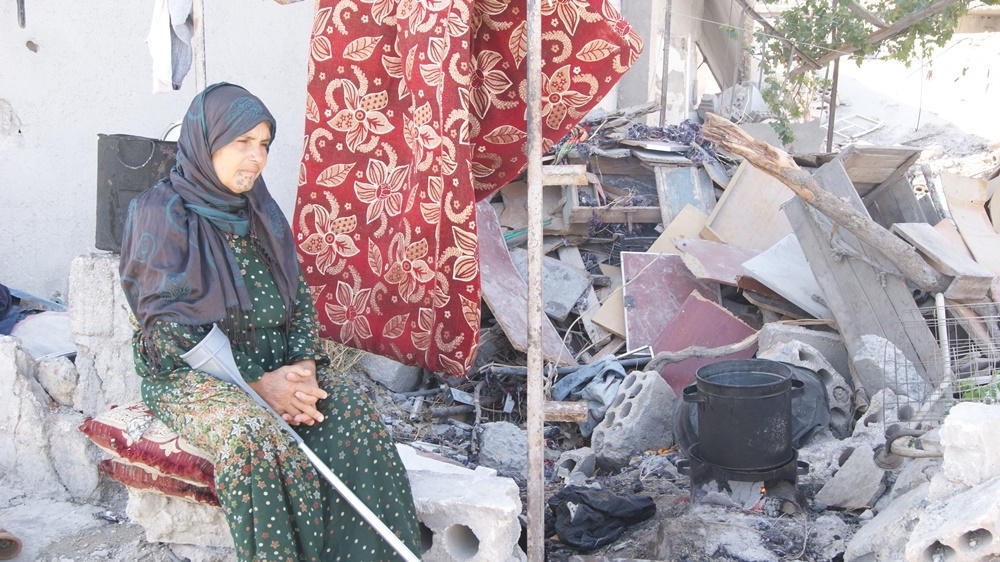 Adla, a Kobane resident who lost a son and grandson in the fight to defend Kobane, sits in front of her partly demolished home [Akhtin Asaad/Al Jazeera]