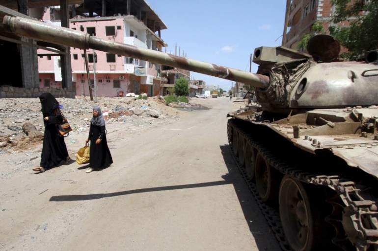 Woman and a girl walk past a broken-down tank on a street in Yemen''s southern port city of Aden