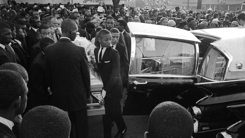 Mourners watch as a group of young pallbearers carry a casket towards a hearse at a funeral for the victims of the Sixteenth Street Baptist Church bombing in Birmingham, Alabama, in 1963. The September 15, 1963 bombing killed four young African American girls - Addie Mae Collins, Cynthia Wesley, Carole Robertson, and Denise McNair [Declan Haun/Chicago History Museum/Getty Images] 