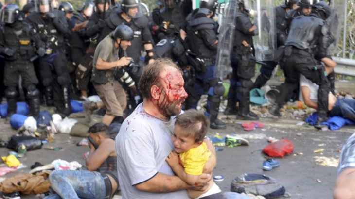 An injured migrant carries a child during clashes with Hungarian riot police at the border crossing with Serbia in Roszke