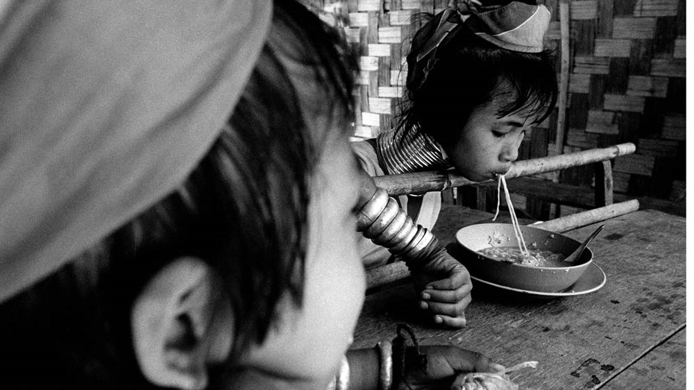 Young Kayan girls at mealtime. The pole supports her head because the coils she wears are heavy [Jack Picone] 