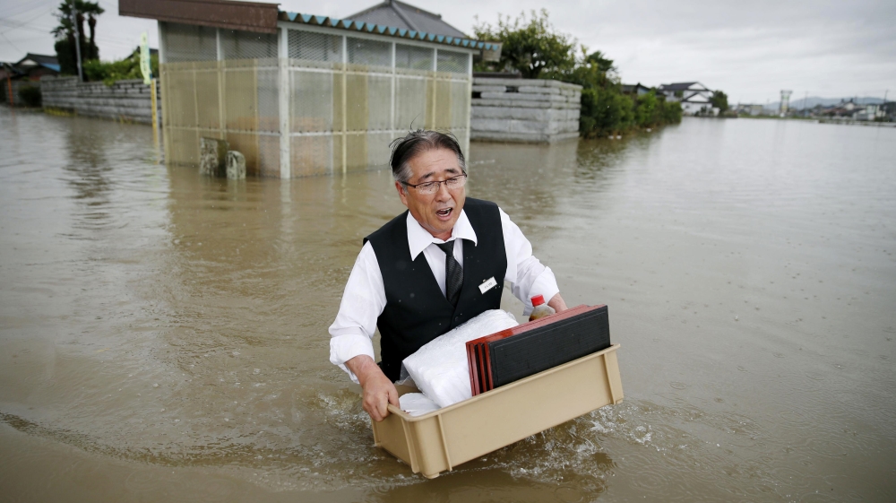 A man carries his belongings through a flooded street in Oyama, northeast of Tokyo on Thursday [Kyodo News/AP] 