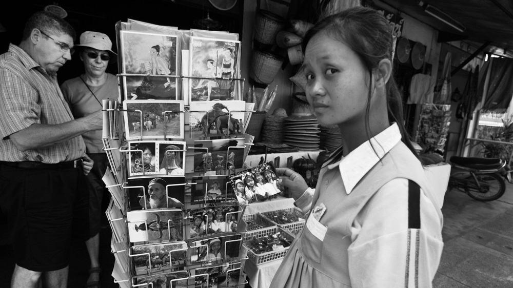 Ma Lo, who has removed her rings, holds a postcard of herself and other long-neck women that is on sale in the town of Mae Hong Son. Ma Lo, who is expecting her second baby, says she was humiliated in the past when the Thais took a photo of her nursing her first child and sold it as a postcard in the town [Jack Picone]